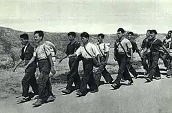Grayscale photograph of Chinese teenagers with backpacks walking down a road.