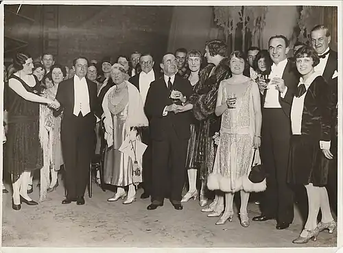Large group photo of people standing, most in evening dress, some holding a drink and/or shaking hands