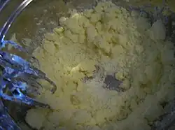 A metal mixing bowl, with chunks of butter and white sugar