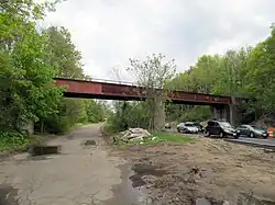 A two-span girder railroad bridge over a section of highway. The left half of the road is disused.